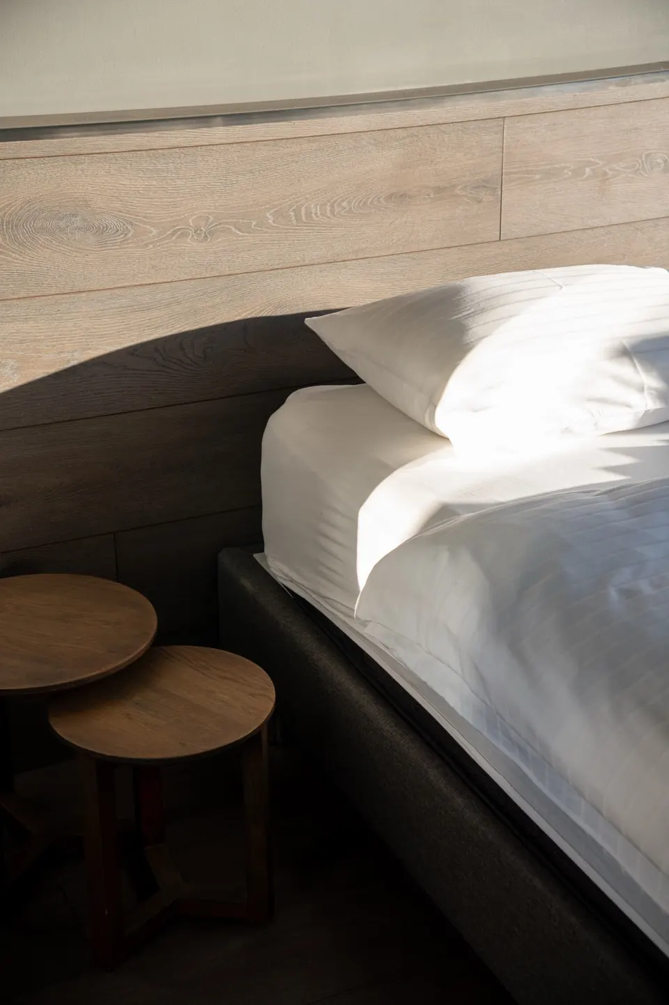 Morning sun on white bed linen against an oak headboard