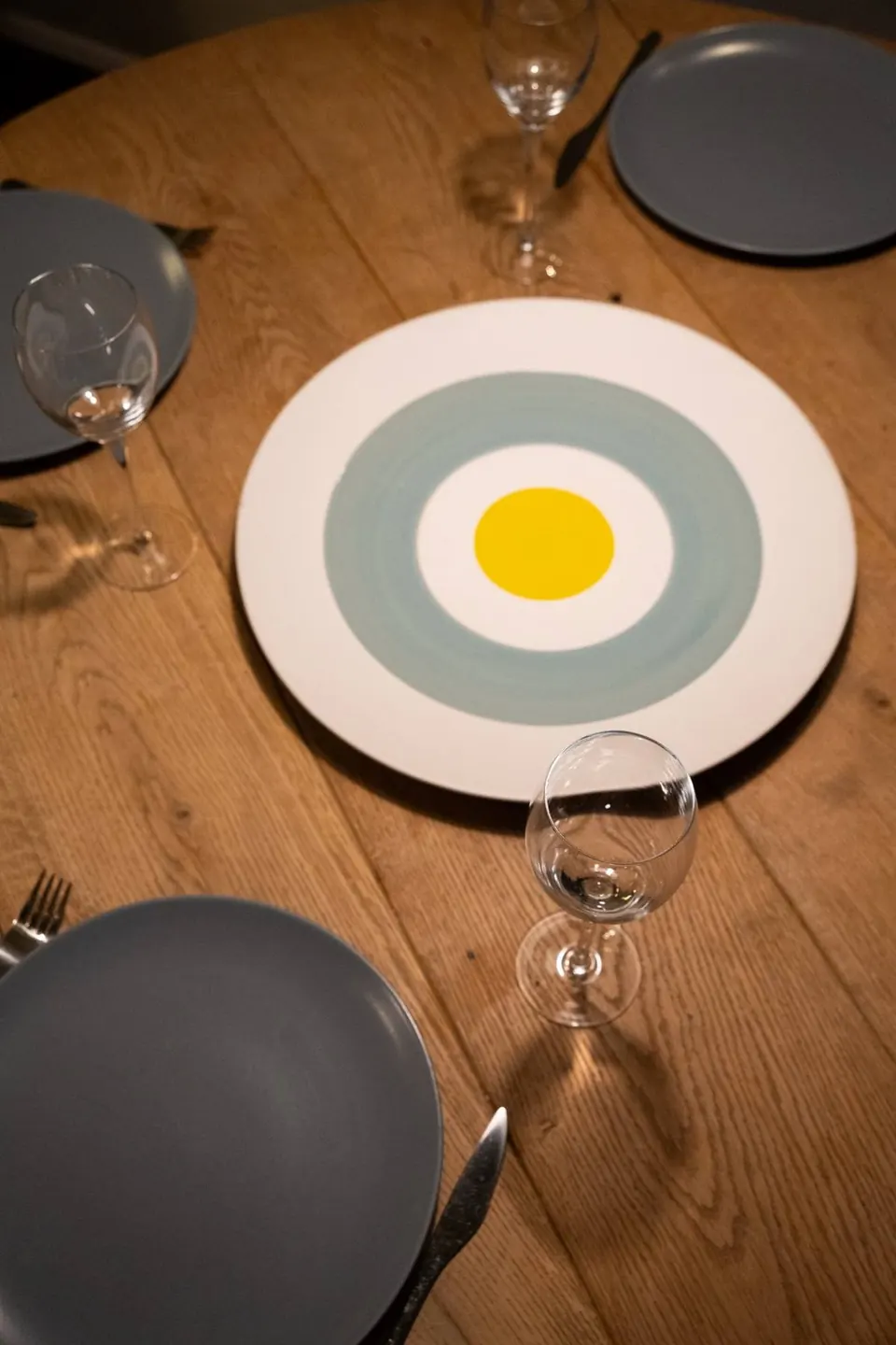 Round oak table laid with grey plates around a white and yellow serving plate